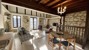 A spacious living area with a stone wall, wooden beams, a fireplace, and a dining table with chairs. - Leonys House in Dhoros (Dhoros)