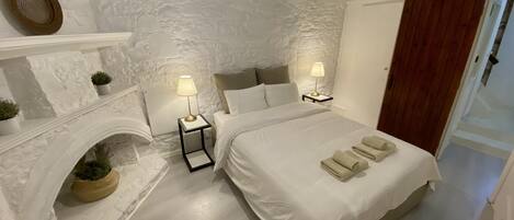 A bedroom with a large bed, two bedside tables with lamps, a fireplace, and a wooden door.