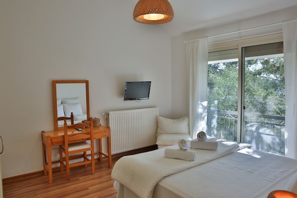 A bedroom with a bed, a desk, a chair, a television, and a window with a view of trees.