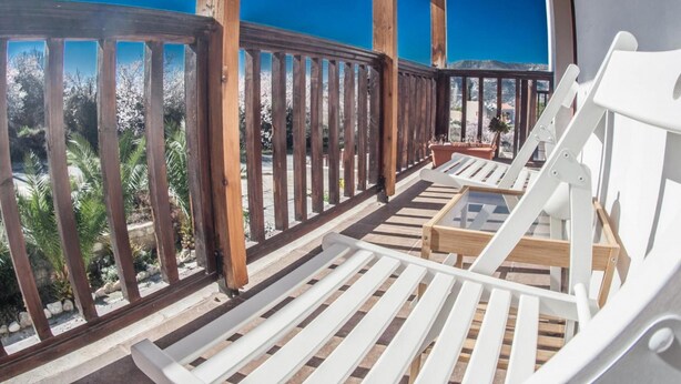 A wooden deck with white lounge chairs and a small table, overlooking a garden and a clear blue sky. - Lania Royal Oak House (Laneia)