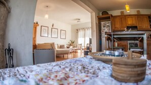 A cozy living room with a sofa, armchairs, and a coffee table. A kitchen with wooden cabinets and appliances is visible in the background. - Lania Royal Oak House (Laneia)