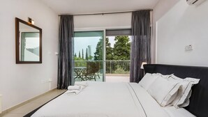 Habitación de hotel moderna con una cama grande, un balcón con mesa y sillas, y vistas a la ciudad.
