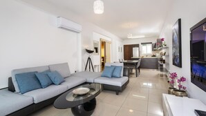 Una sala de estar moderna con un sofá seccional gris, una mesa de centro de vidrio y un comedor con una mesa y sillas blancas.
