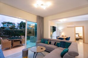 Ein modernes Wohnzimmer mit einer Couch, einem Couchtisch und einem Essbereich mit Stühlen. Eine Glastür führt zu einem Balkon mit Gartenmöbeln.