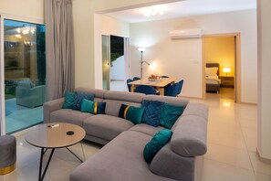 Una sala de estar moderna con un sofá seccional gris, una mesa redonda y un comedor con una mesa y sillas.
