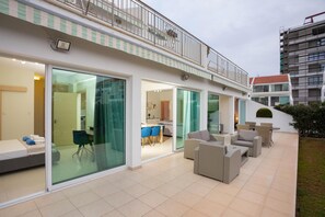 Un apartamento moderno con balcón, grandes puertas correderas de vidrio y zona de patio con mobiliario exterior.