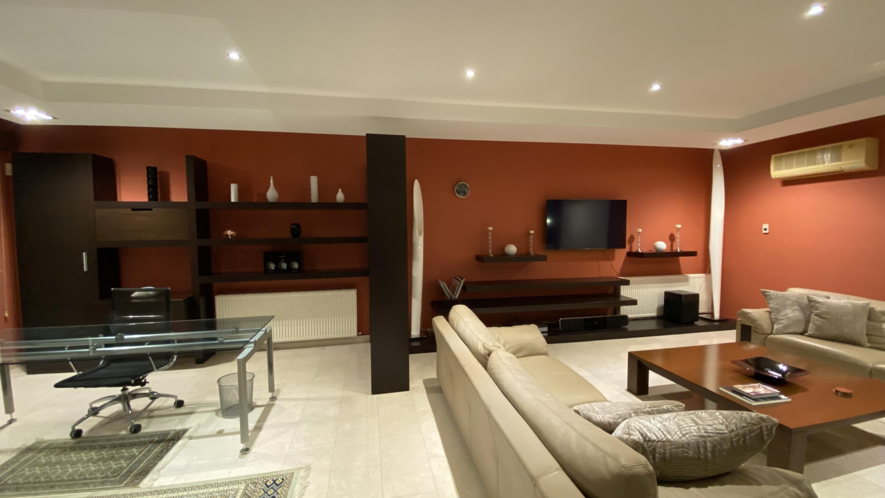 A modern living room with a sofa, coffee table, TV, and shelves with decorative items.