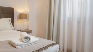 A neatly made bed with a rolled white towel, a bedside lamp, and sheer curtains. - Kanika Seabreeze Apartment (Limassol)