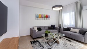 A modern living room with a grey sofa, a glass coffee table, and a colorful abstract painting on the wall. - Kanika Seabreeze Apartment (Limassol)