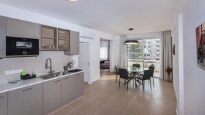 A modern kitchen with a built-in microwave, a sink, and cabinets. There is a dining area with a table and chairs, and a balcony with a view of the city. - Kanika Seabreeze Apartment (Limassol)