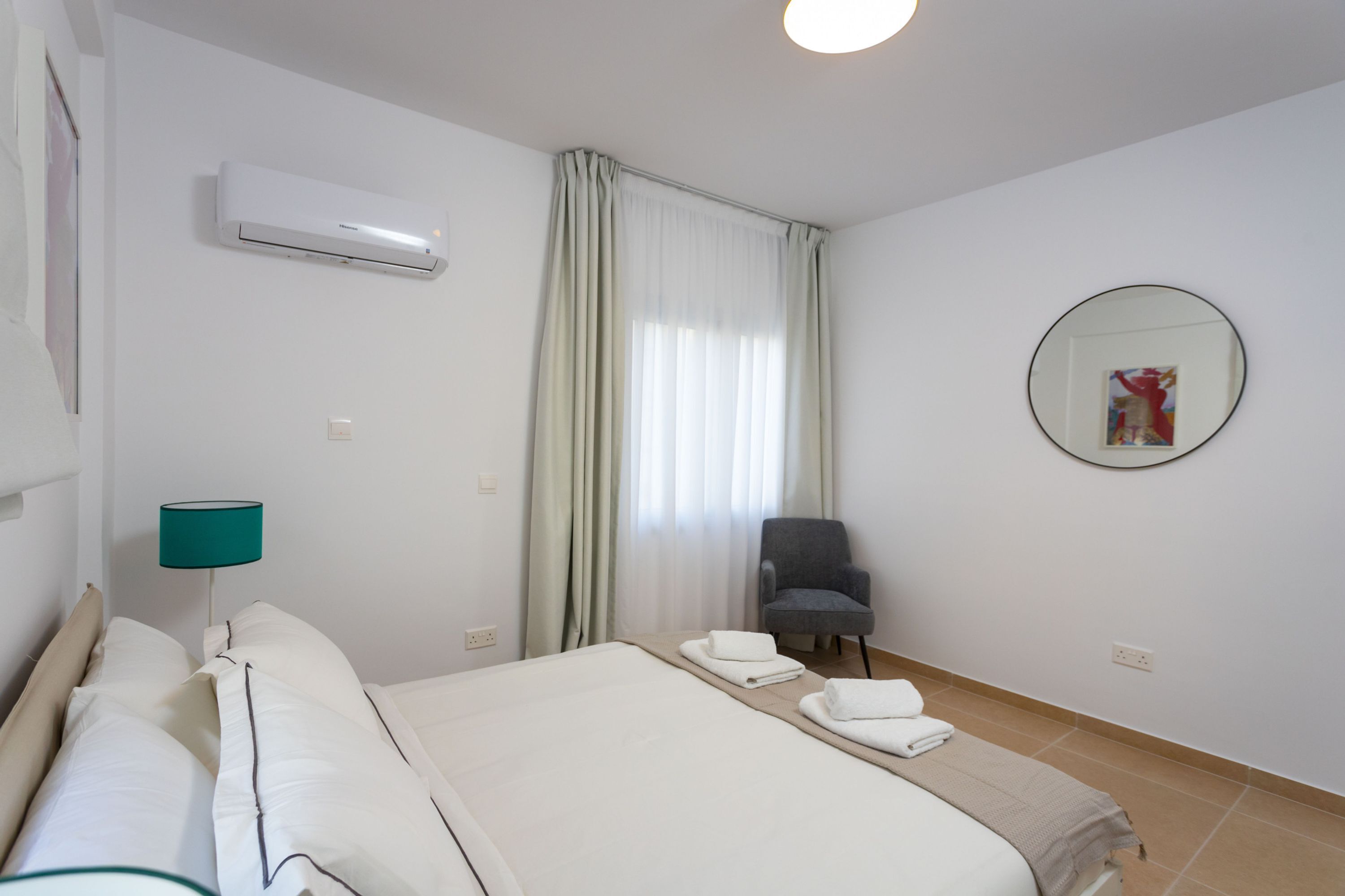 Habitación de hotel con cama, una silla, una lámpara, aire acondicionado y una ventana con cortinas.