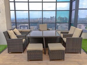 Relax in this outdoor seating area with a glass table and six comfortable chairs, surrounded by a city view.