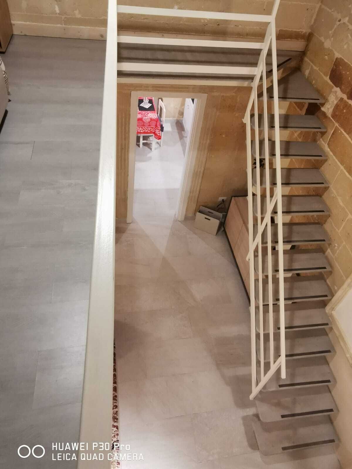 Una escalera con barandilla blanca que lleva a un cuarto con mantel rojo estampado.