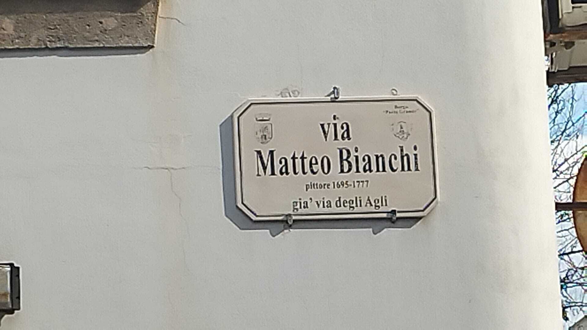 A street sign reading "Via Matteo Bianchi" with the years "1695-1777" and "via degli Agl" below.