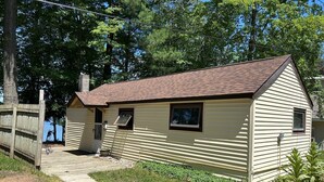 A small, single-story cabin with a sloped roof, a front porch, and a small window. - Cottage with Private Beach on Spider Lake - Free Kayaks, Canoe & Pedal Boat! (Traverse City)