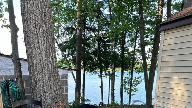 A glass-top table with metal chairs, a potted plant, and a view of a lake. - Cottage with Private Beach on Spider Lake - Free Kayaks, Canoe & Pedal Boat! (Traverse City)