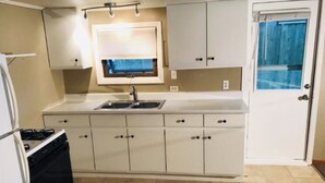 A compact kitchen with a gas stove, a sink, and a window with a view of a blue sky. - Cottage with Private Beach on Spider Lake - Free Kayaks, Canoe & Pedal Boat! (Traverse City)