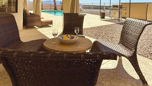 Un coin salon aménagé avec des meubles en osier, comprenant une table ronde, un saladier rempli de fruits et deux verres à vin.
