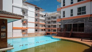 Una piscina con la inscripción 'New Nordic' en el agua, rodeada de edificios de varios pisos con balcones y un cielo azul despejado.
