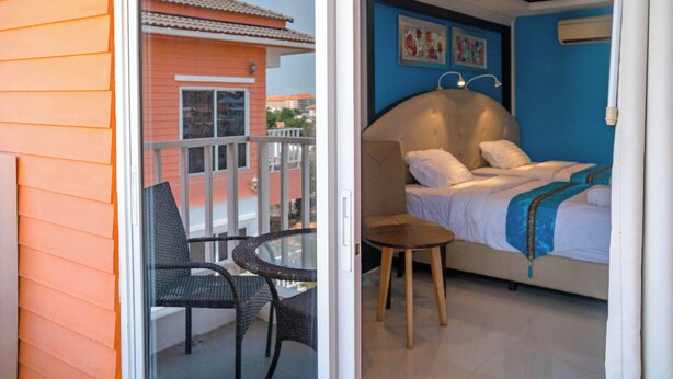 Una habitación con una cama, una mesita y una silla. Hay un balcón con barandilla y vistas a un edificio.