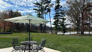An outdoor patio with a round table and chairs, a striped umbrella, and a view of a lake and trees.