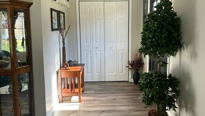 A hallway with a wooden floor, a white door, a small table with a vase, and a potted plant.