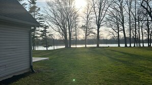 A grassy yard with a house on the left and a lake in the background.