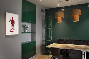 Un espace repas moderne avec une table en bois, des étagères vertes et deux lampes suspendues.