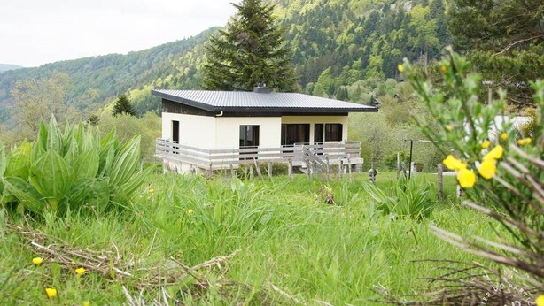 A small, single-story cabin with a sloped roof, surrounded by lush greenery and a forested hillside. - Mountain chalet   (Mont-Dore)