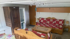 A compact living space with a wooden sofa, a small table, a wooden chair, and a bed with a floral bedspread. - Mountain chalet   (Mont-Dore)