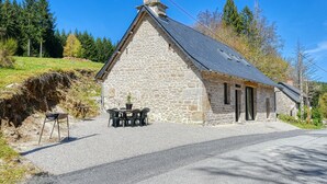 Un edificio de piedra con techo inclinado, una chimenea y un pequeño espacio al aire libre con una mesa y sillas.