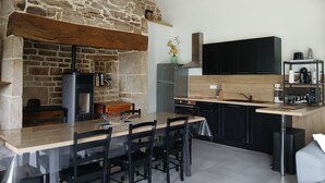Una cocina con pared de piedra, techo de madera y zona de comedor con sillas y una mesa.