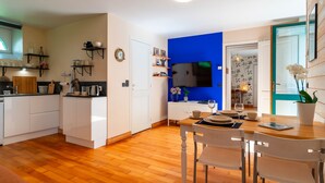 A modern kitchen with white cabinets, a wooden dining table, and a blue accent wall. - Le Relais - Maison avec grand jardin (Bannalec)