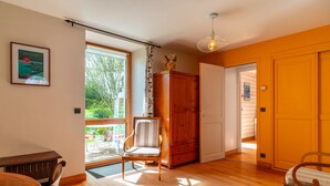 A spacious room with a wooden floor, a dining table, a chair, a cabinet, and a door leading to another room. - Le Relais - Maison avec grand jardin (Bannalec)