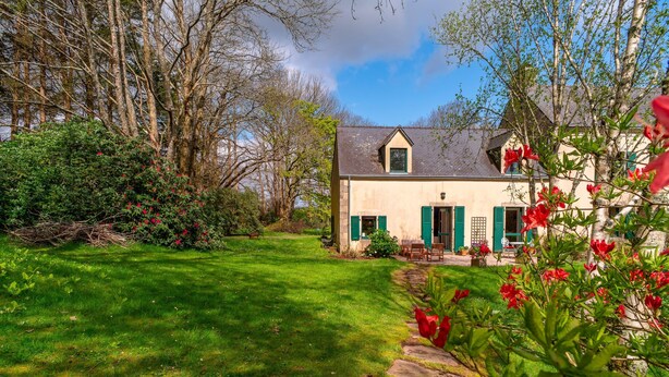 A house with a stone pathway leading to the entrance, surrounded by lush greenery and trees. - Le Relais - Maison avec grand jardin (Bannalec)