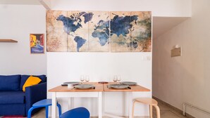 A dining area with a wooden table, two blue chairs, and a world map artwork above.