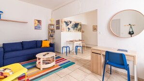 A living room with a blue sofa, a small round table, a colorful striped rug, and a desk with a chair.
