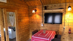 A cozy cabin interior with a wooden wall, a TV mounted above a table, and a door leading to another room.