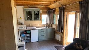 A compact kitchen with a sink, cabinets, and a small refrigerator. There is a dog resting on a chair in the living area.