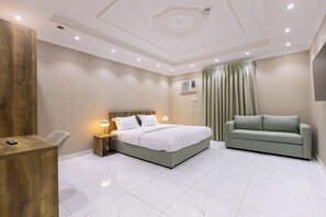 A hotel room with a bed, a green sofa, a desk, and a TV. - Al-Rajhi - Qaswarah Residence (Madinah)