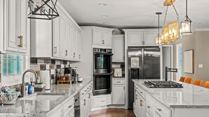 A modern kitchen with white cabinetry, a large island, stainless steel appliances, and pendant lighting. - Estate: Heated Pool, Hot Tub, Game Rooms, Pets (La Grange)