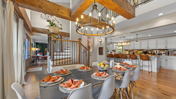 A spacious dining area with a large table set for six, surrounded by modern chairs. A chandelier hangs from the ceiling, and a staircase leads to an upper level. The kitchen in the background features white cabinets and a central island. - Estate: Heated Pool, Hot Tub, Game Rooms, Pets (La Grange)
