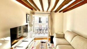 Un salon confortable avec une télévision, un canapé et un balcon doté d’une balustrade en fer forgé.
