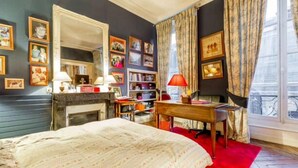 Une chambre à coucher avec un lit, un bureau, une chaise, une bibliothèque et une fenêtre avec des rideaux.