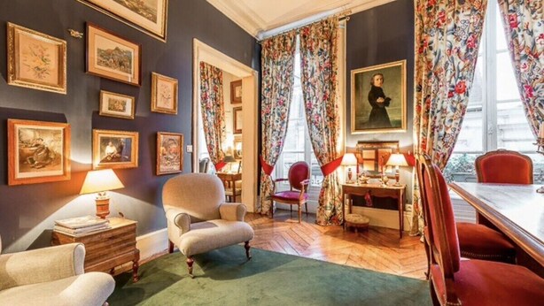 Une pièce avec une moquette verte, une table en bois, une chaise rouge et un portrait encadré accroché au mur.