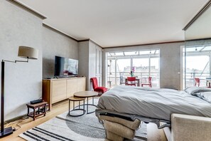 Una habitación de hotel moderna con una cama grande, un televisor sobre un mueble de madera, una mesita redonda y una silla roja.