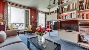 Un salon avec un canapé, une table basse sur laquelle est posé un vase, un téléviseur et une bibliothèque.