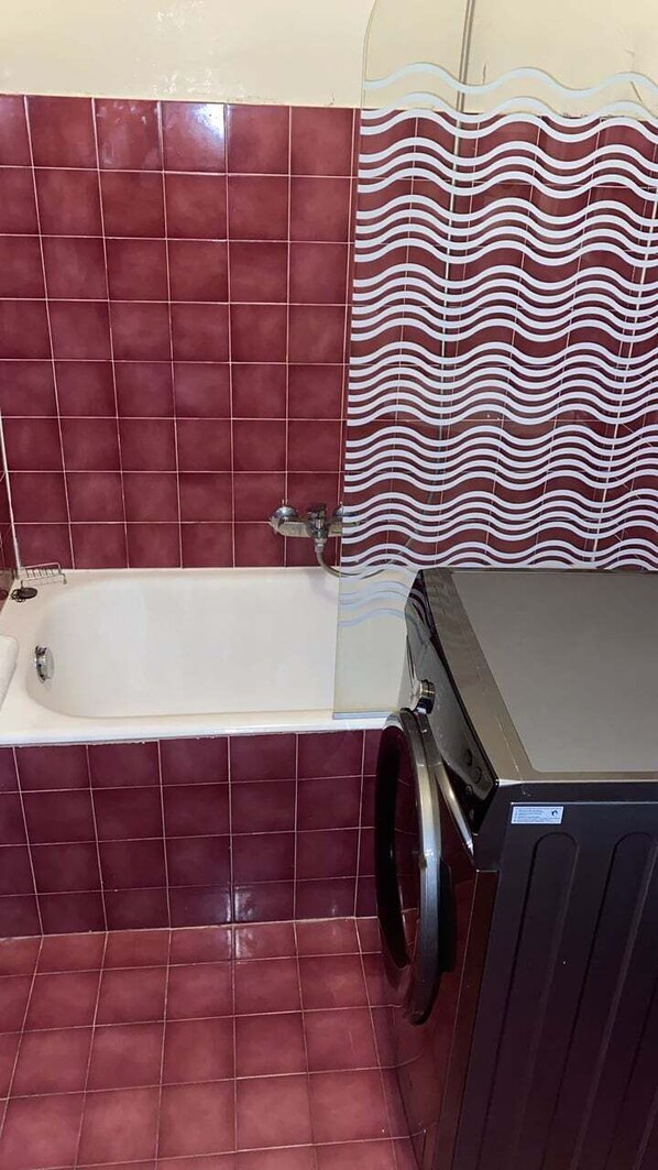 Een badkamer met een bad, een wasmachine en een betegelde muur.