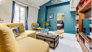 A living room with a sofa, armchair, and coffee table. There is a bed in the adjacent room with a blue wall. - The architect - Design & Luxurious (Paris)