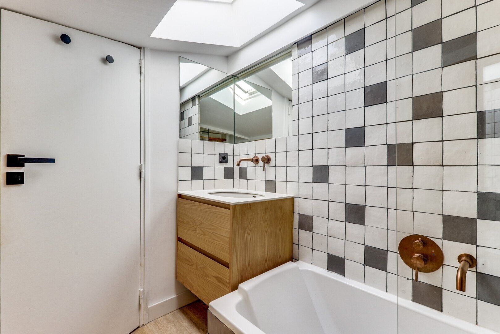 Een moderne badkamer met dakraam, een houten wastafelmeubel en een bad.
